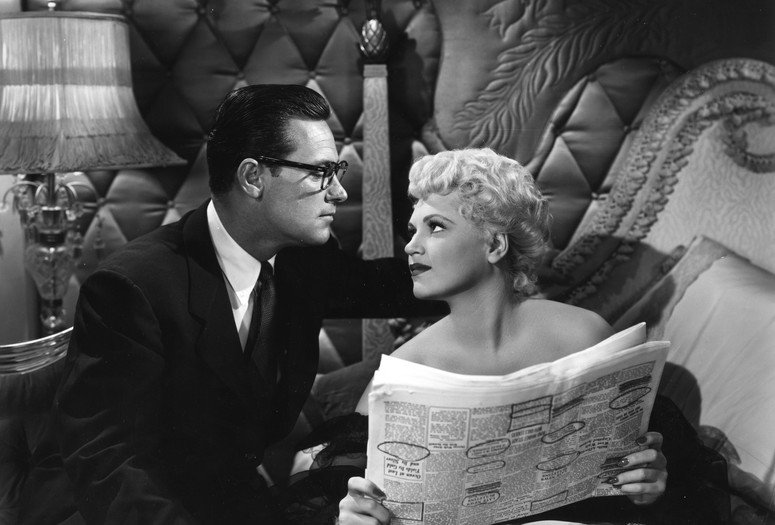 A woman stares up at a man while holding an open newspaper