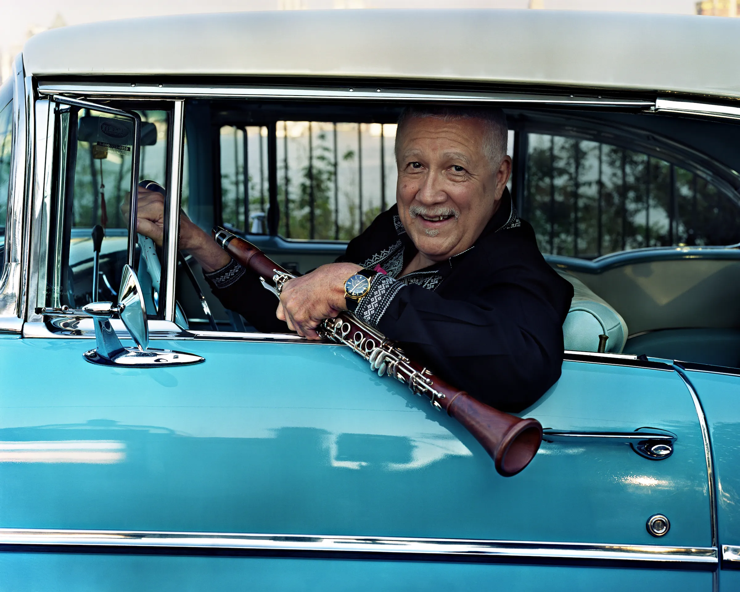 Musician Paquito D'Rivera sits in a parked car holding a clarinet