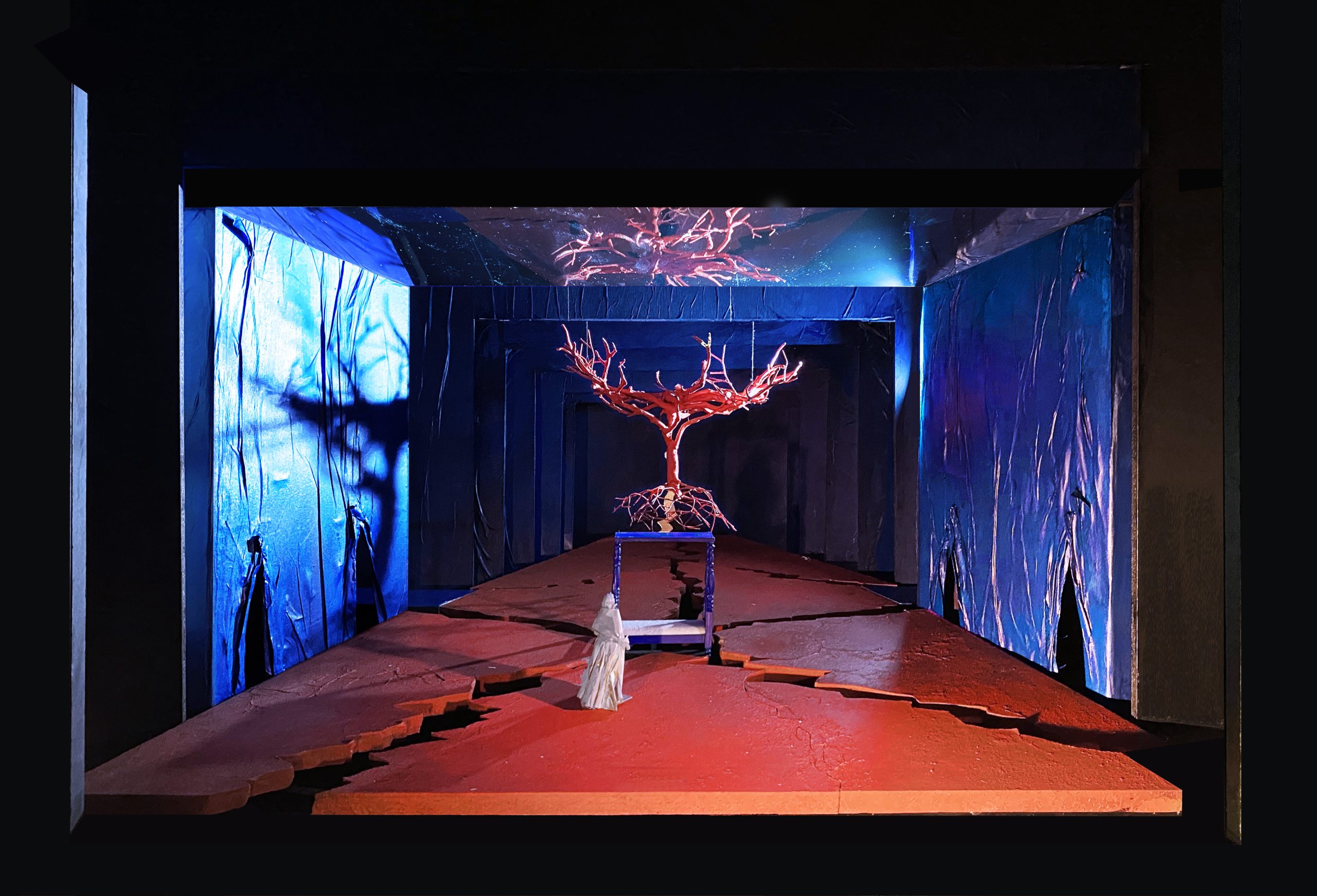 An empty stage lit in blue and red, with a tree sculpture floating in the center
