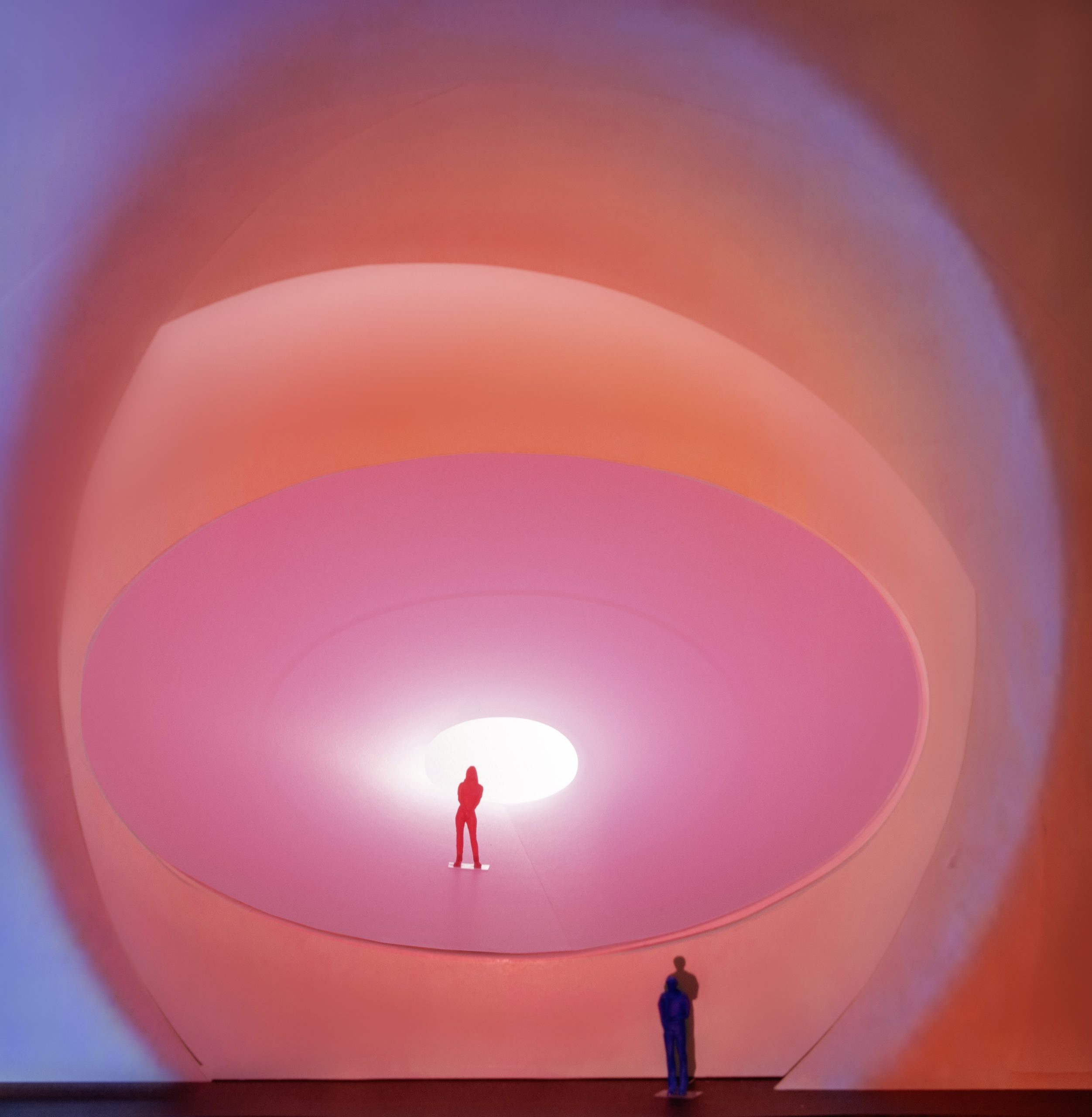Two statues stand against a vibrant pink background