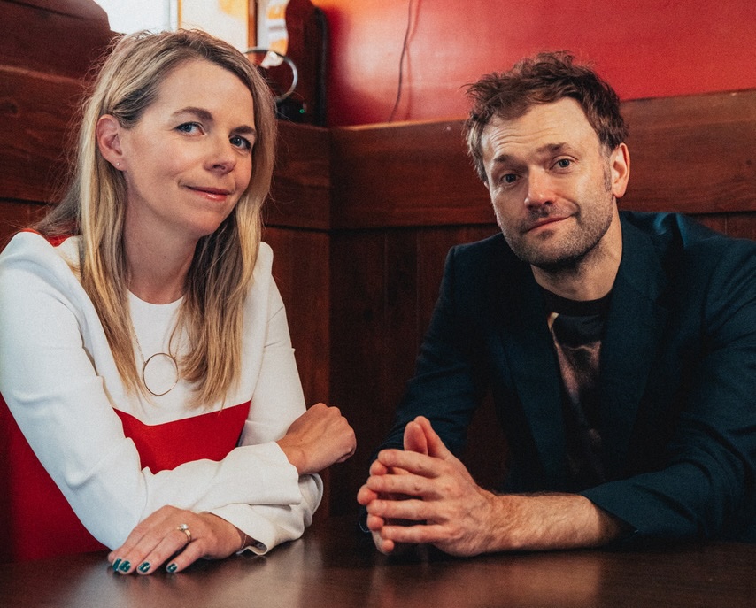 Musicians Aoife O'Donovan and Chris Thile seated together inside at a table