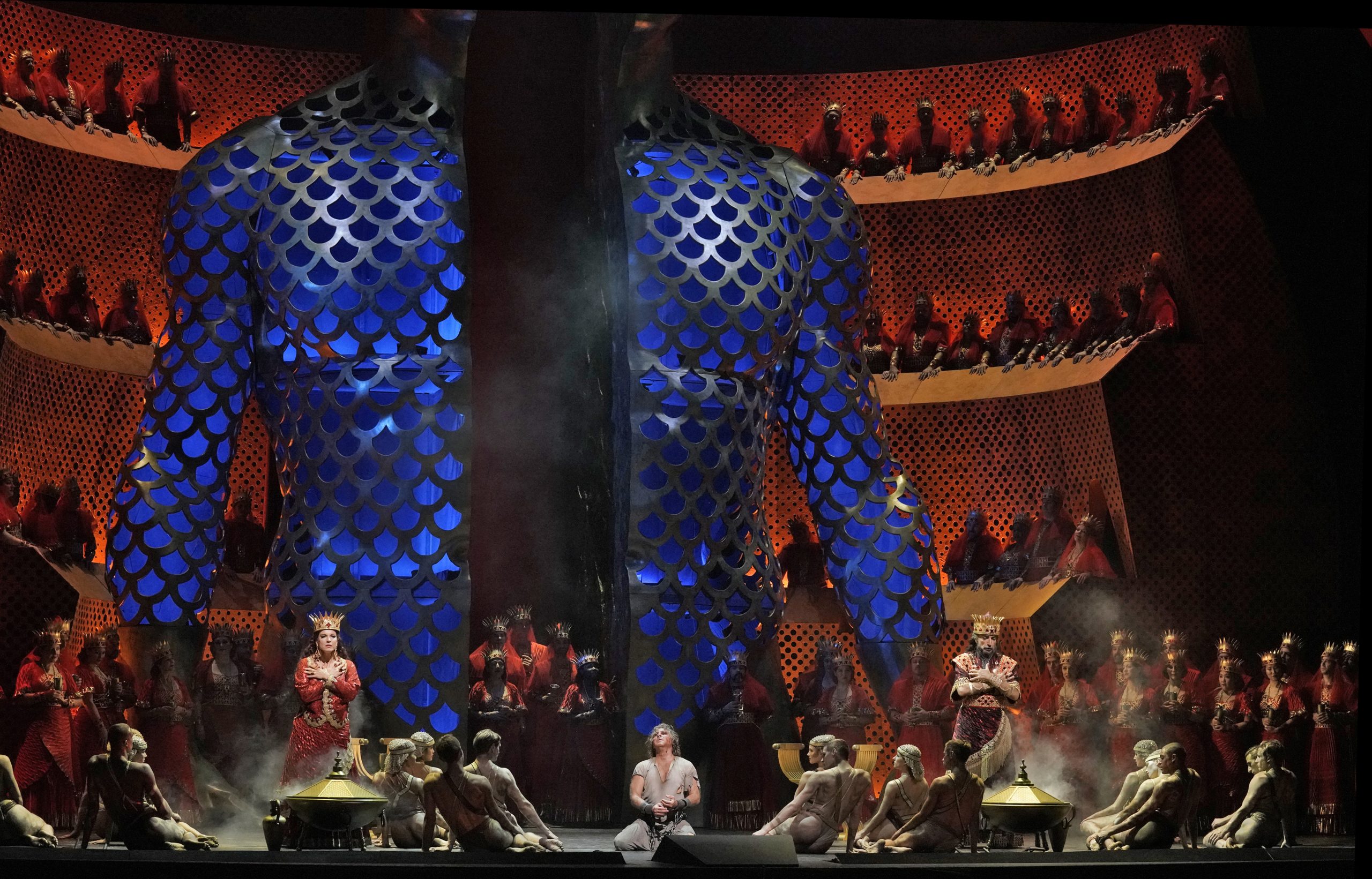 A large bust of a torso on a stage with people surrounding a prisoner in the center