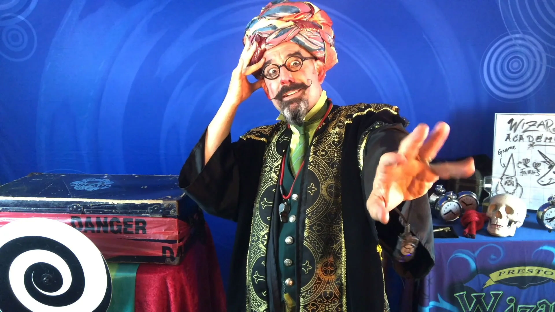 A man dressed as a wizard in front of a blue spiral backdrop promoting a family friendly theater production